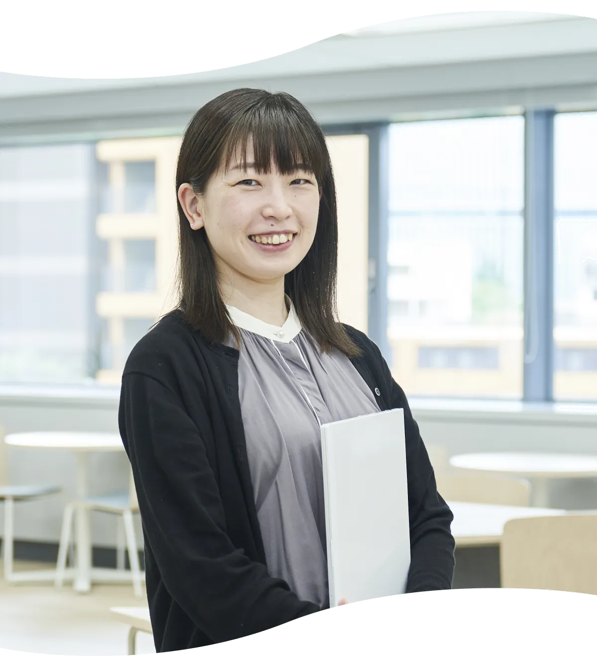 資料を手に窓辺で微笑む計算技術開発部のM.M