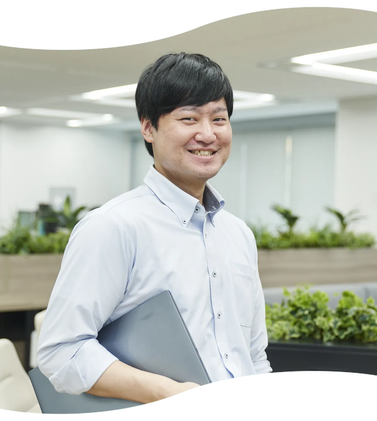 オフィスでノートパソコンを手に微笑むITソリューション部のT.M
